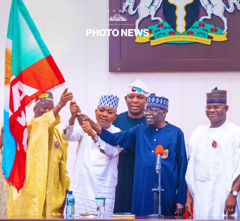 President Tinubu, supported by Dr Ganduje hands APC flag to Ododo as Gov Bello looks on.